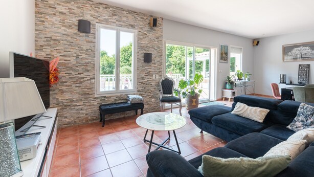A spacious living area with a stone wall, a dark blue sofa, a glass coffee table, and a bench. - Holiday Home 'Maison Zoé' with Private Pool, Private Terrace and Wi-Fi (Saint-Laurent-de-Neste)
