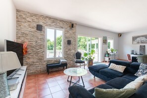 Un vaste espace de vie agrémenté d’un mur en pierre, d’un canapé bleu foncé, d’une table basse en verre et d’un banc.