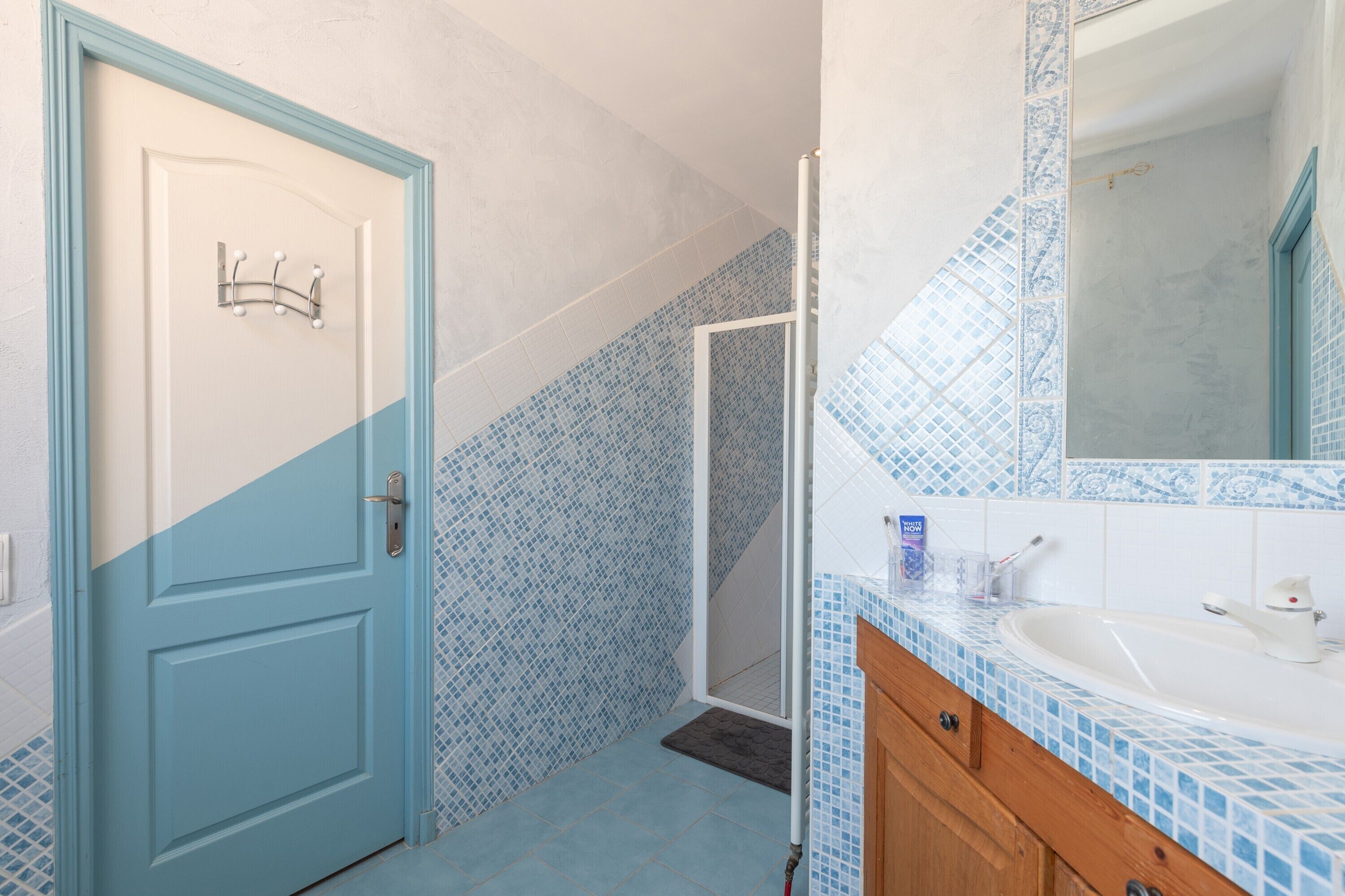 Un bagno con una porta blu, una doccia, un lavandino con specchio e pareti piastrellate.