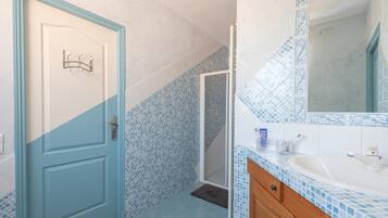 Un bagno con una porta blu, una doccia, un lavandino con specchio e pareti piastrellate.
