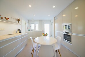 A modern kitchen with white cabinets, a white dining table with four chairs, and a built-in oven. - Villa 'Amarna' with Sea View, Wi-Fi and Air Conditioning (La Herradura)