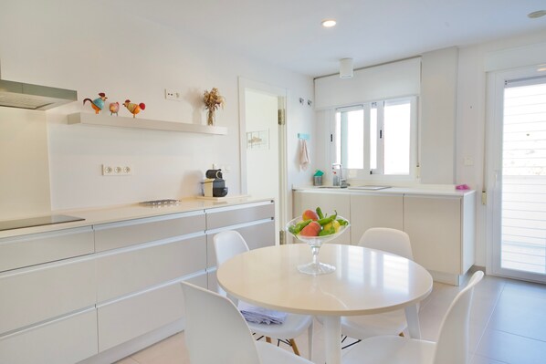 A modern kitchen with white cabinetry, a round dining table, and a fruit bowl.