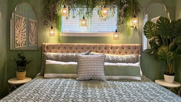 Een slaapkamer met een gestoffeerd hoofdeinde, beddengoed met een patroon en hangplanten.