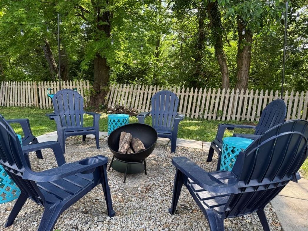 An outdoor seating area with six Adirondack chairs and a fire pit.