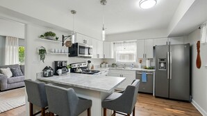 Een moderne keuken met witte kasten, een centraal eiland met barkrukken, een roestvrijstalen koelkast en een koffiehoek.