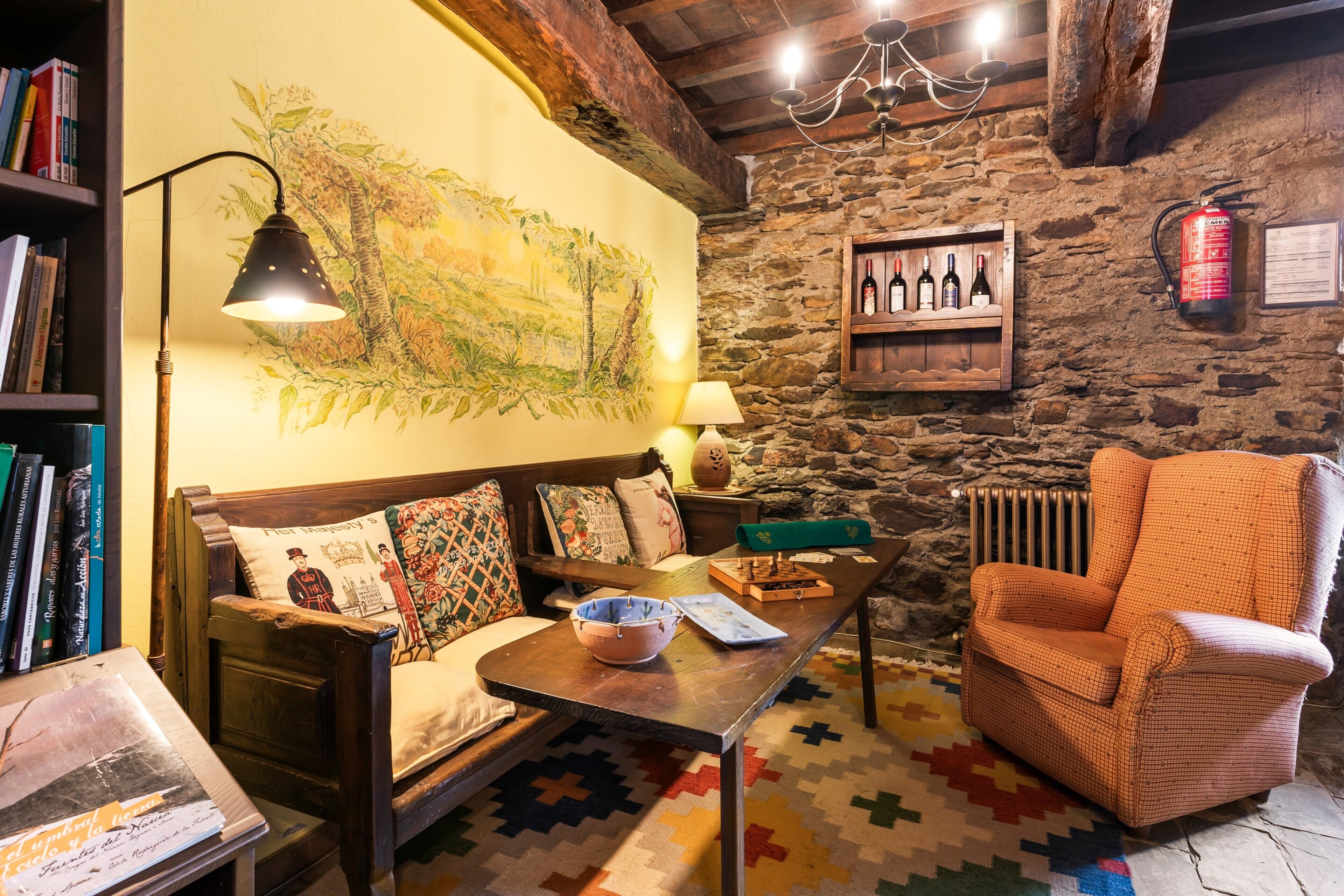 Una habitación acogedora con un sofá de madera, una alfombra estampada, una mesa con un cuenco, una silla, una estantería, un cuadro en la pared y una pared de piedra.