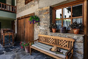 Un edificio in pietra con una panchina di legno, piante in vaso e una finestra con tende.