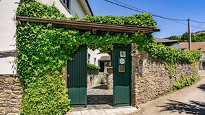 Um edifício de pedra com porta verde e entrada coberta, rodeado por vegetação.