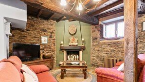 Uma sala de estar acolhedora com uma parede de pedra, lareira, televisão e um sofá vermelho.