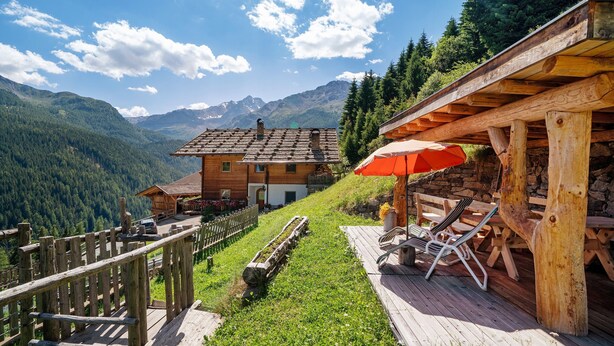Un chalet en bois doté d’une terrasse, de chaises longues et offrant une vue sur les montagnes.