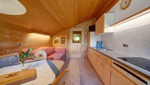 L’intérieur chaleureux d’un chalet avec un plafond en bois, un coin repas comprenant une table et des chaises, une petite cuisine équipée d’une cuisinière, et une porte donnant sur une autre pièce.