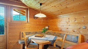 L’intérieur d’un chalet en bois comprend une table à manger, des chaises, un banc, un luminaire suspendu et une fenêtre.