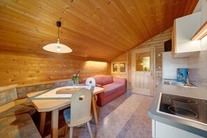 A wooden interior with a dining table, a sofa, a kitchen area with a stove, and a door leading to another room.
