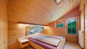 Une chambre dans une cabane en bois, avec un lit, une petite table de chevet, une fenêtre donnant sur l’extérieur et une porte.