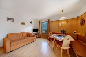 A room with a sofa, dining table, chairs, a TV, and a window with curtains.