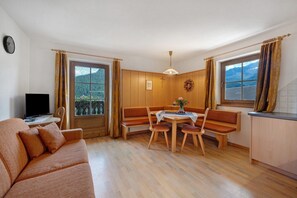A room with a sofa, a dining table with chairs, a television, and a window with curtains.