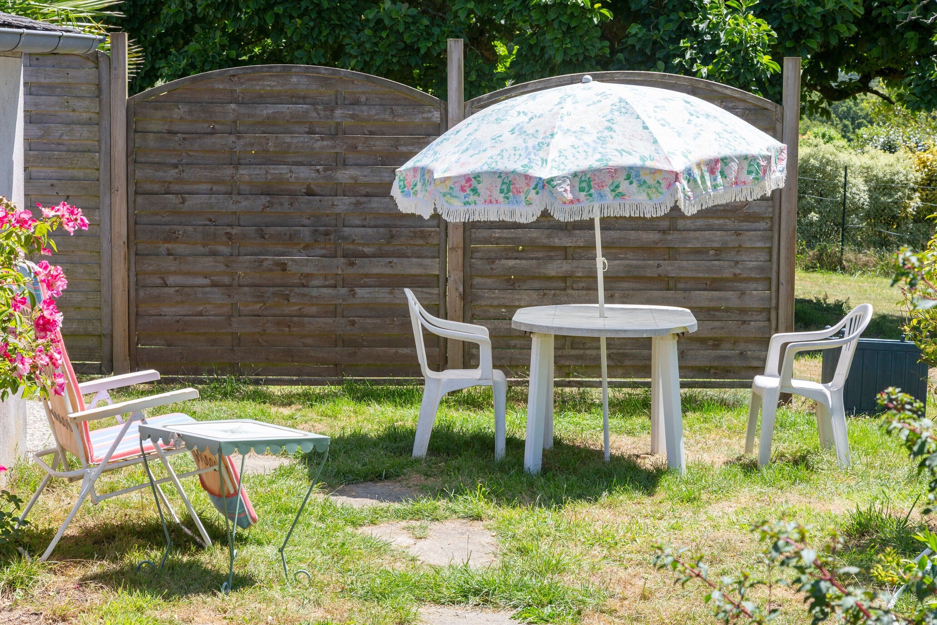 A patio with a table and two chairs, an umbrella, and a wooden fence in the background.