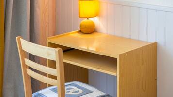 A wooden desk with a lamp, a chair with a cushion, and a wall with paneling.