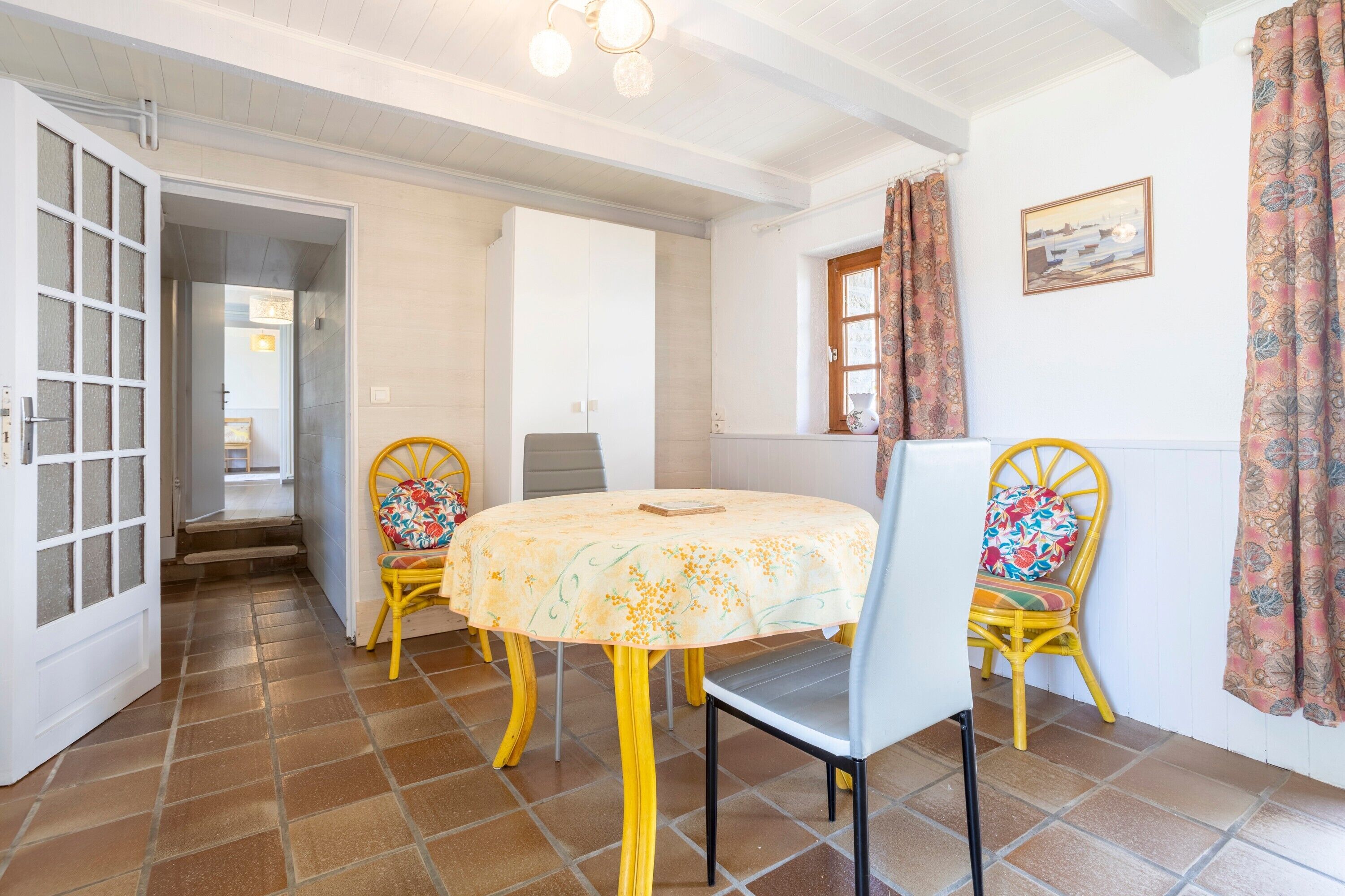 A dining area with a round table, two chairs, a door, and a window with curtains.