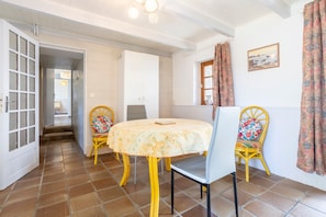 A dining area with a round table, two chairs, a door, and a window with curtains. - Holiday Home 'Ty Bihan' with Private Terrace and Private Garden (Rosporden)