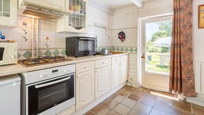 Una cocina con armarios blancos, microondas, estufa y ventana con cortina.