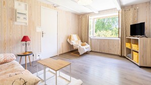 Una habitación con paredes de madera, una cama, una mesa, una silla, un televisor y una ventana con vistas.