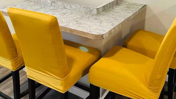 A dining area with a marble countertop and four yellow chairs.