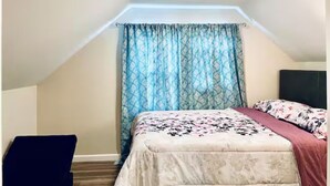 Une chambre avec un plafond en pente, un lit recouvert d’une couvre-lit à motifs floraux et un rideau bleu à motifs.