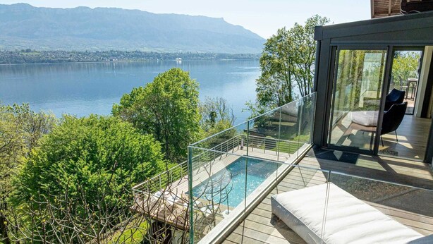 A modern villa with a glass-enclosed balcony overlooking a lake, a hot tub, and a seating area with a view of the mountains. - LA LEZARDIERE DU LAC (BOURDEAU)