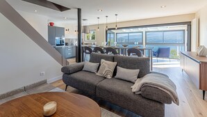 A modern living room with a grey sofa, wooden coffee table, and a dining area with a view. - LA LEZARDIERE DU LAC (BOURDEAU)