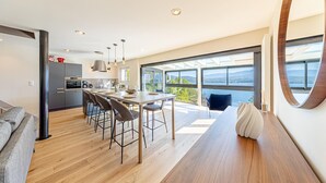 A modern kitchen with a central island, bar stools, and a dining area with a view of the outdoors. - LA LEZARDIERE DU LAC (BOURDEAU)