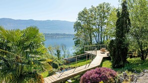 A wooden deck with a railing overlooking a lake, surrounded by lush greenery and trees. - LA LEZARDIERE DU LAC (BOURDEAU)