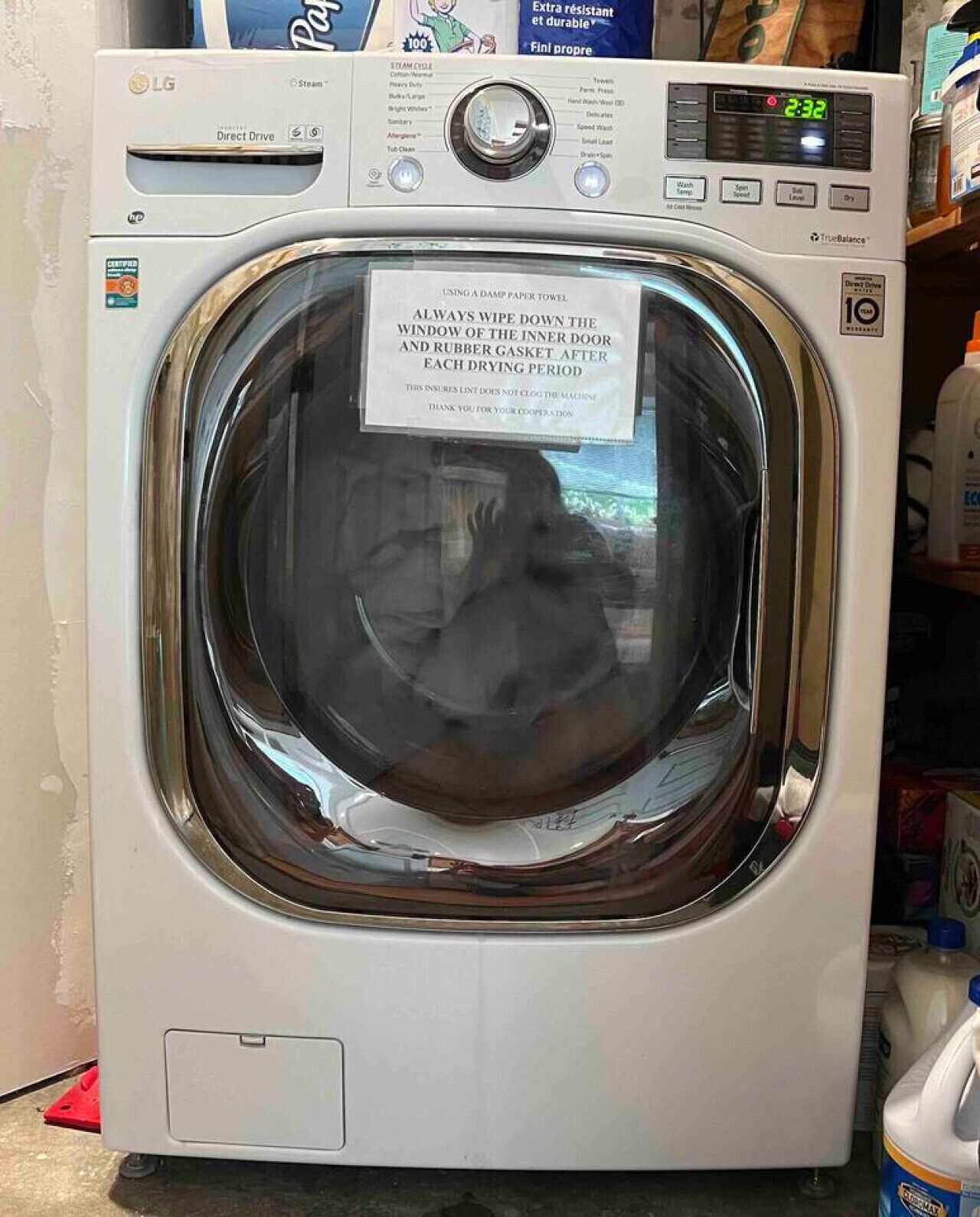 Un lave-linge à chargement frontal doté d’un écran numérique et d’une notice indiquant qu’il faut essuyer la vitre et le joint en caoutchouc après chaque cycle de séchage.