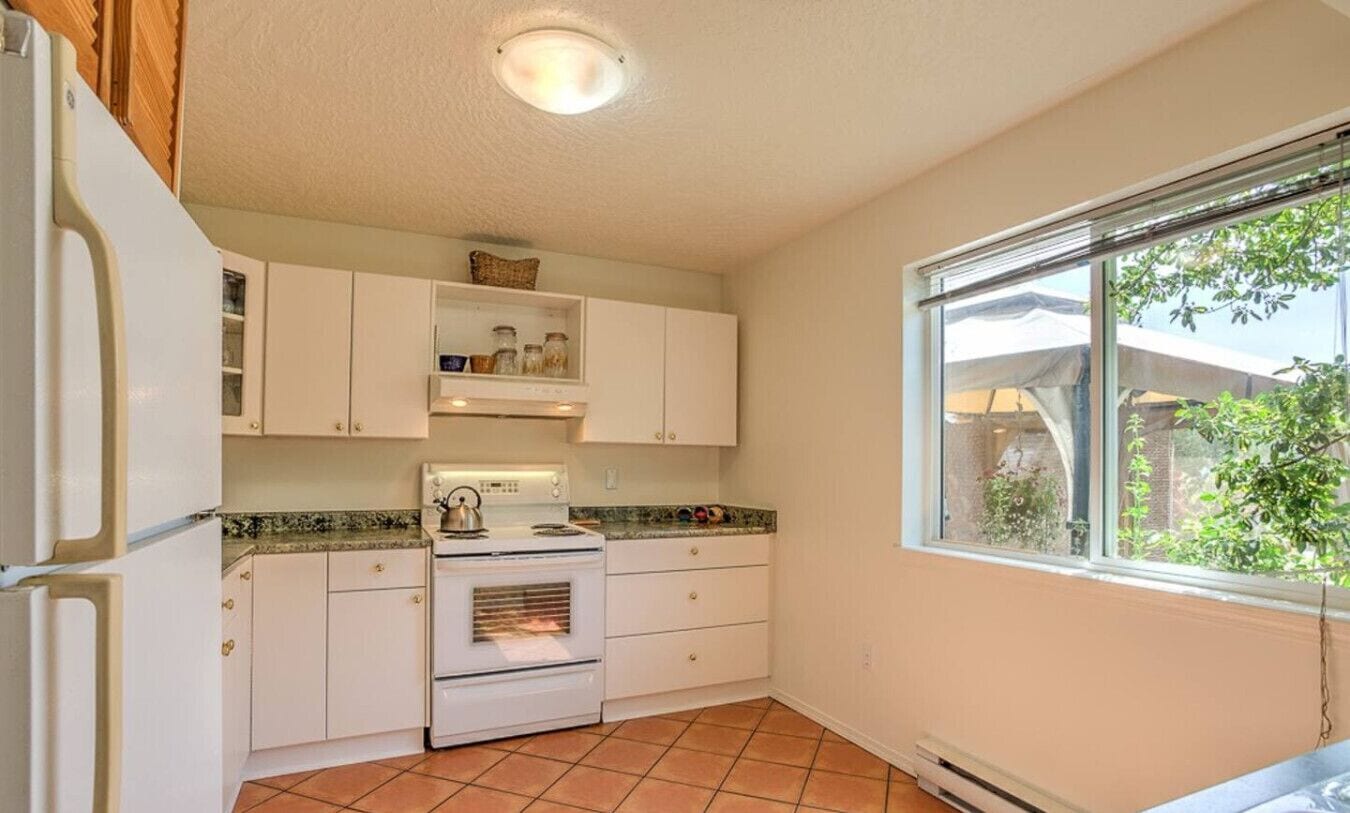 A compact kitchen with white cabinets, a stove, and a window with a view of greenery.