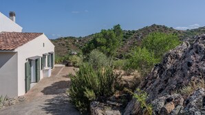 A white building with a tiled roof, a paved pathway, and a rocky hillside in the background. - Holiday Home 'Maya' with View Over the Hills, Private Terrace and Wi-Fi (Olbia)