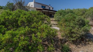 A house with a sloped roof, surrounded by dense shrubbery and a clear blue sky. - Holiday Home 'Maya' with View Over the Hills, Private Terrace and Wi-Fi (Olbia)