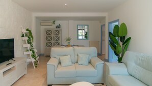 Ein modernes Wohnzimmer mit einem hellblauen Sofa, einem Couchtisch mit Dekoration, einem Fernseher auf einer weißen Kommode und einer Treppe mit Pflanzen.