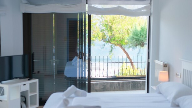Ein Hotelzimmer mit Bett, Fernseher, Glastür zu einem Balkon mit Blick auf Bäume und Geländer.