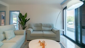 Ein modernes Wohnzimmer mit einem hellen Sofa, einem Couchtisch und einem großen Fenster mit Jalousien.