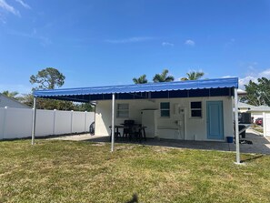 A covered outdoor area with a table and chairs, a door, and a white fence. - Cozy Retreat with Private Backyard (Naples)