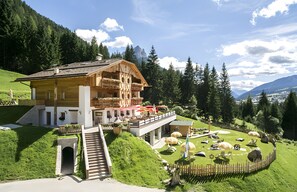 A chalet with a balcony, a staircase, and a garden with sheep statues.