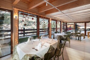 A dining area with tables set for a meal, large windows with decorative lights, and a view of a mountainous landscape.
