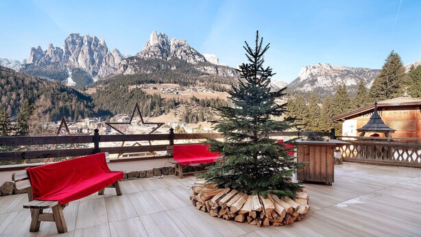 Une terrasse en bois, un sapin de Noël, des chaises rouges et une vue sur les montagnes.
