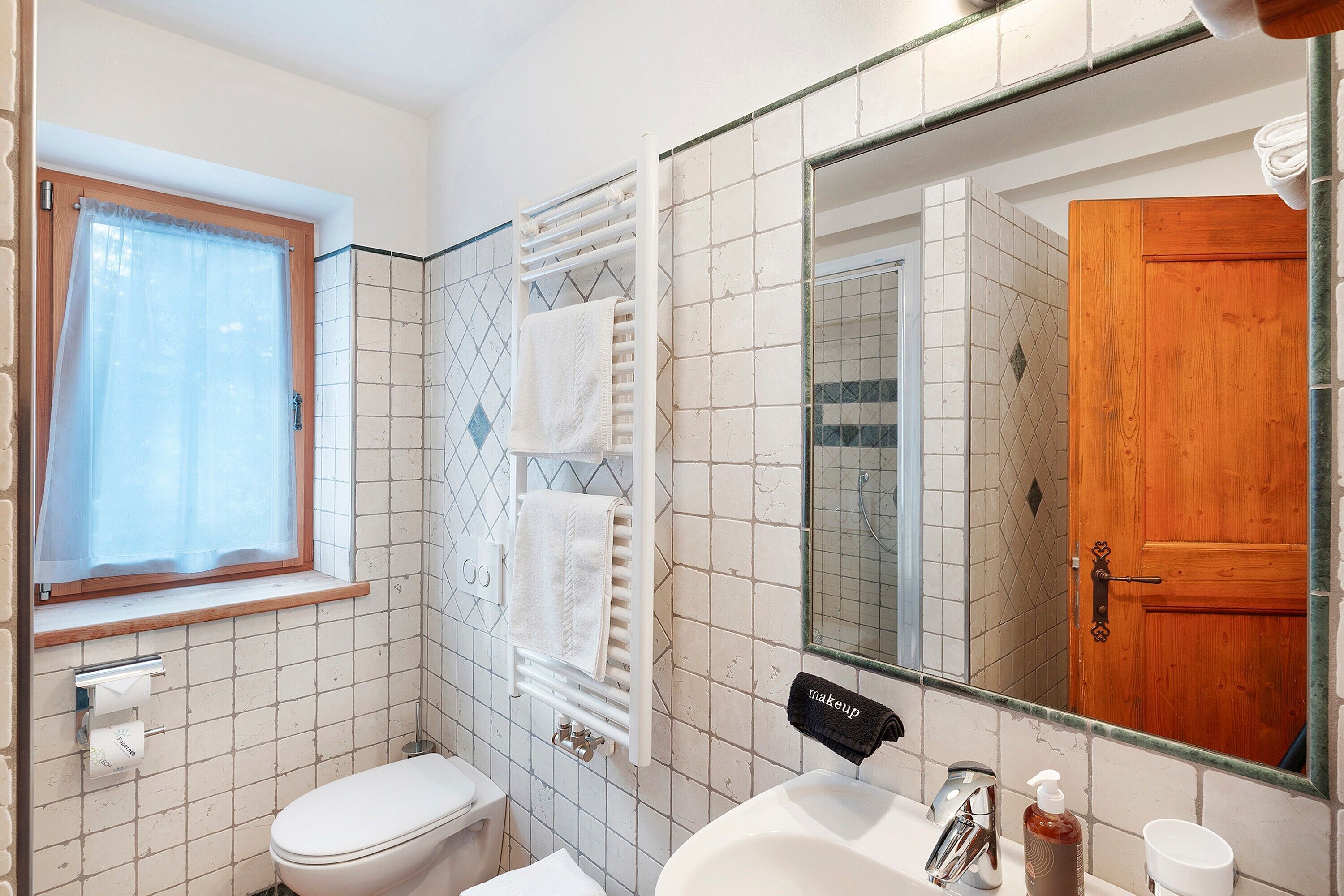 A bathroom with a toilet, sink, mirror, and towel rack.