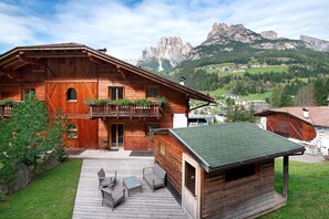 Een houten chalet met een balkon, terras en uitzicht op de bergen.