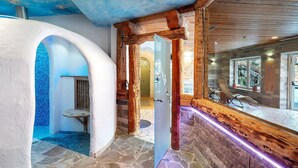 Un couloir au sol en pierre, avec des poutres en bois, une porte en verre et un coin salon offrant une vue agréable.