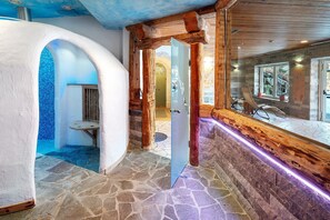 A stone-floored hallway with wooden beams, a glass door, and a seating area with a view.