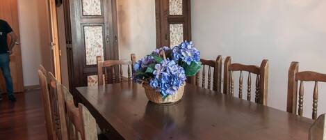 A dining area with a wooden table, chairs, a chandelier, and a floral centerpiece.