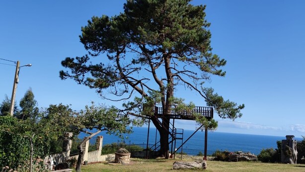 A tree with a wooden platform, a clear sky, and a distant view of the sea. - Villa 'Quintes' with Sea View, Private Terrace and Wi-Fi (Villaviciosa)