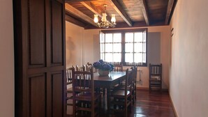 A dining area with a wooden table and chairs, a chandelier, and a view through a window. - Villa 'Quintes' with Sea View, Private Terrace and Wi-Fi (Villaviciosa)